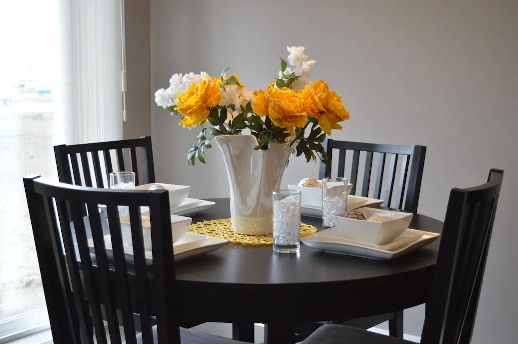 Round dining table made of dark wood with four chairs and a bouquet of white and orange flowers in the center.