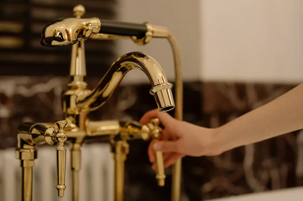 A beautiful golden faucet with a hand on the handle.