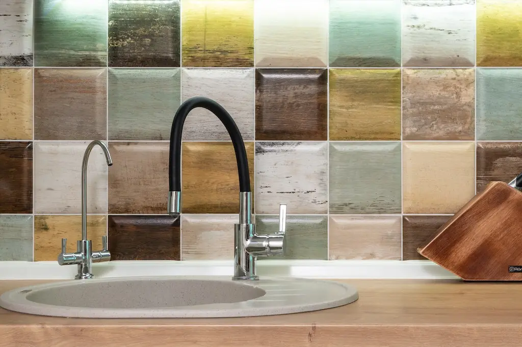 A nice kitchen faucet in front of a beautiful marbled wall.